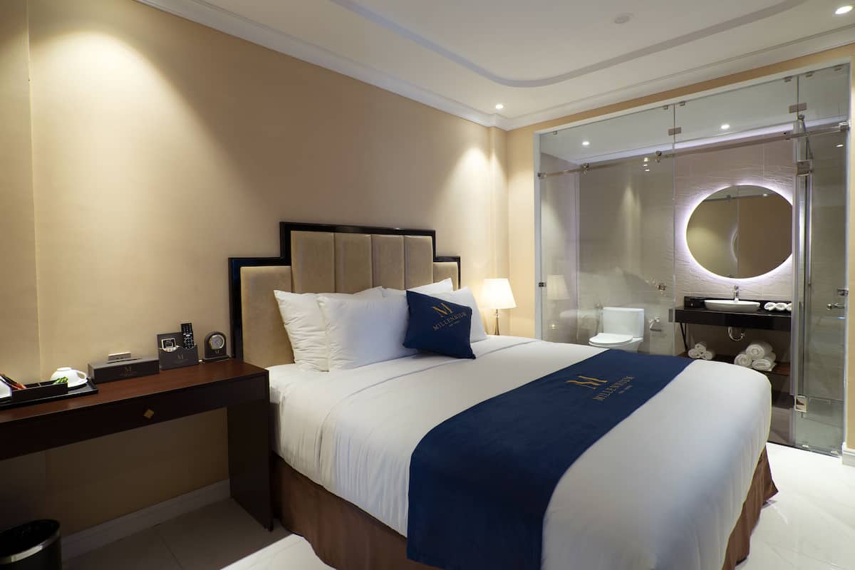 A hotel room with a large bed, a desk with a telephone, and a glass-enclosed shower area.