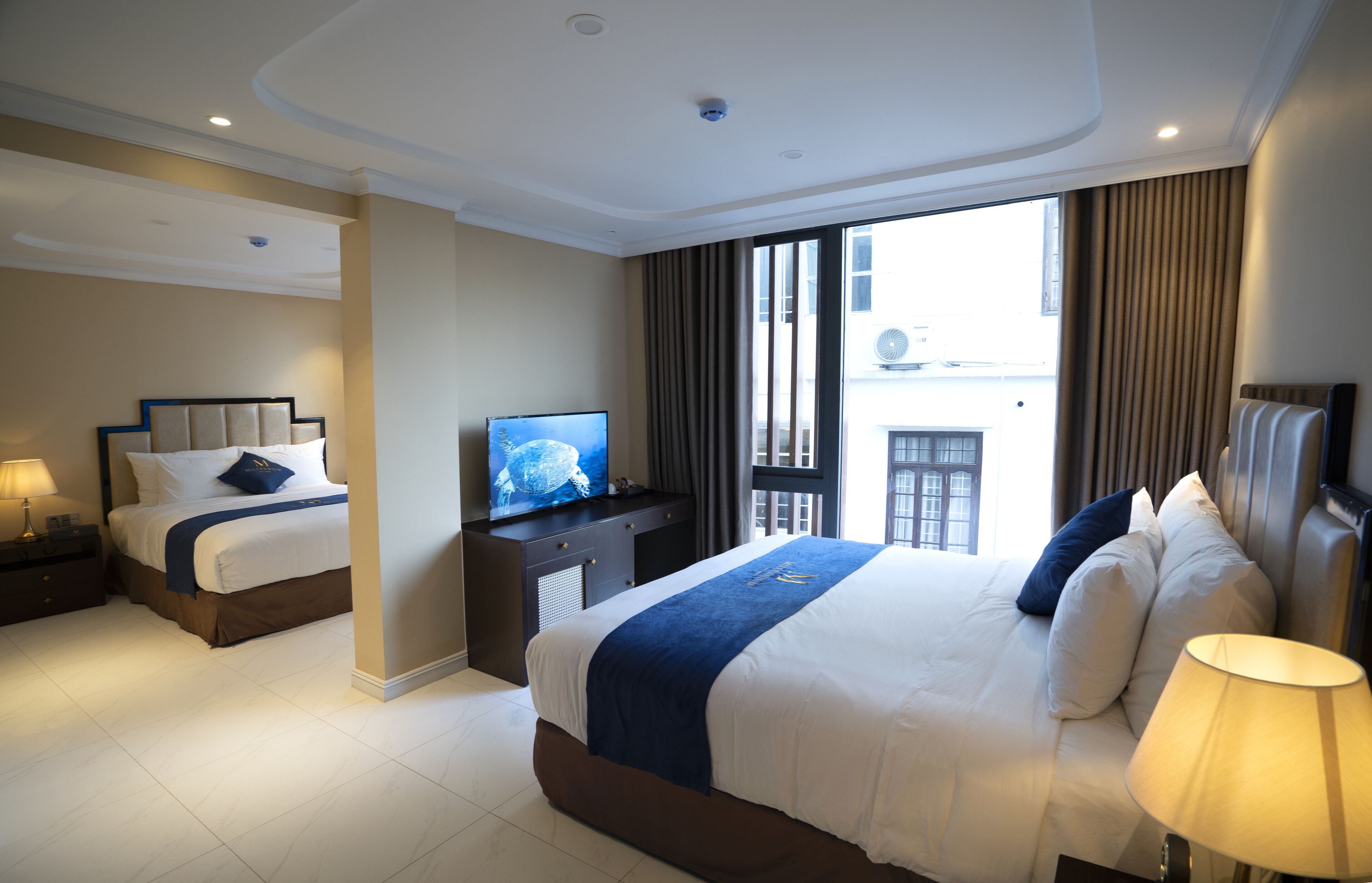 A hotel room with a large bed, a smaller bed, a TV, a desk, and a window with curtains.