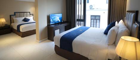 A hotel room with a large bed, a smaller bed, a TV, a desk, and a window with curtains.