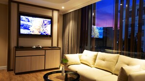 Una sala de estar moderna con un sofá, una mesa de centro, un televisor montado en la pared y vistas de la ciudad a través de ventanas amplias.
