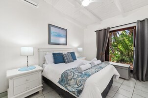 A bedroom with a bed, nightstands, a window with curtains, a ceiling fan, and a wall-mounted picture.