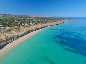 An aerial view of a coastal town with a long sandy beach, clear turquoise waters, and a backdrop of hills. - Rose Villa - Port Willunga Beach Retreat (Port Willunga)