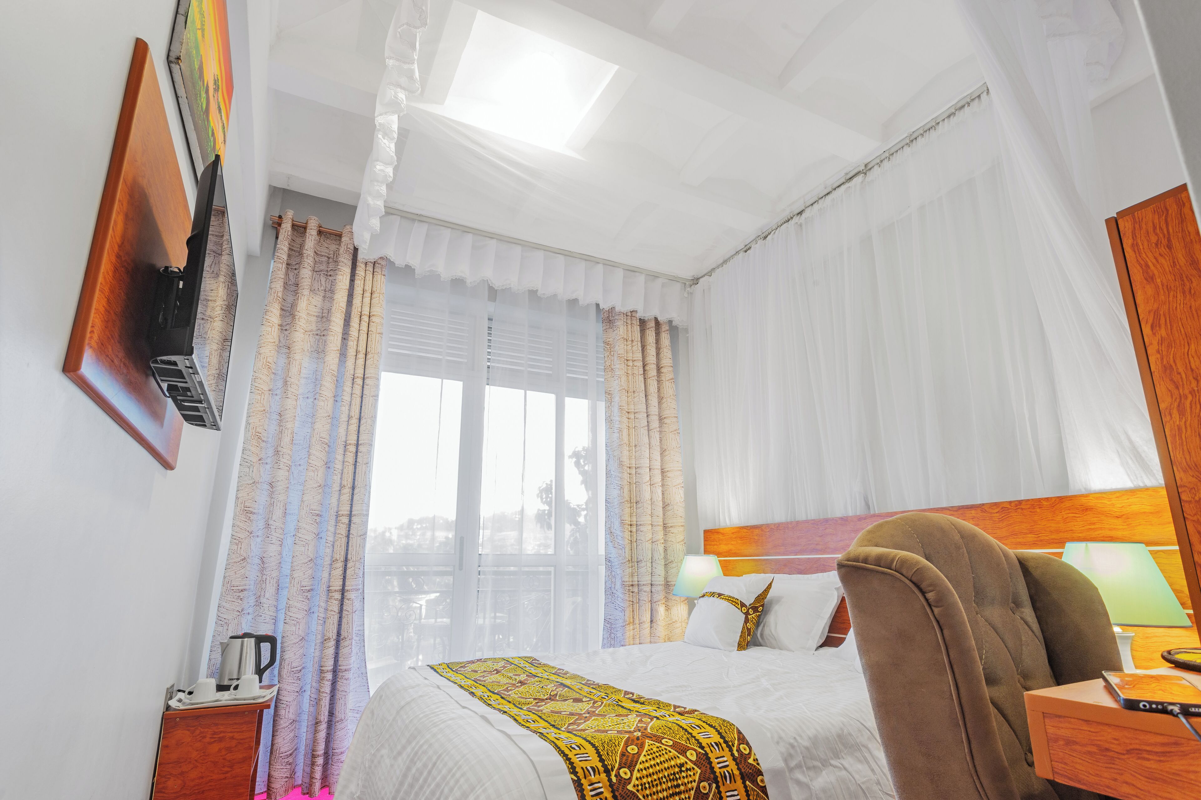 A hotel room with a bed, a desk, a chair, a TV, and a window with curtains.