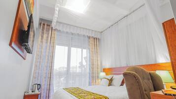 Habitación de hotel con cama, escritorio, silla, televisor y ventana con cortinas.
