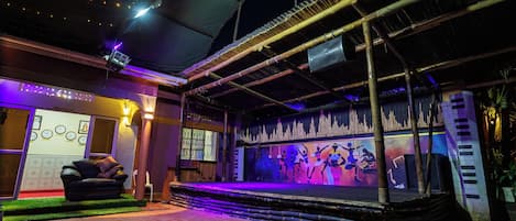 An outdoor stage with a performance area, a reception desk, and a seating area with a sofa.