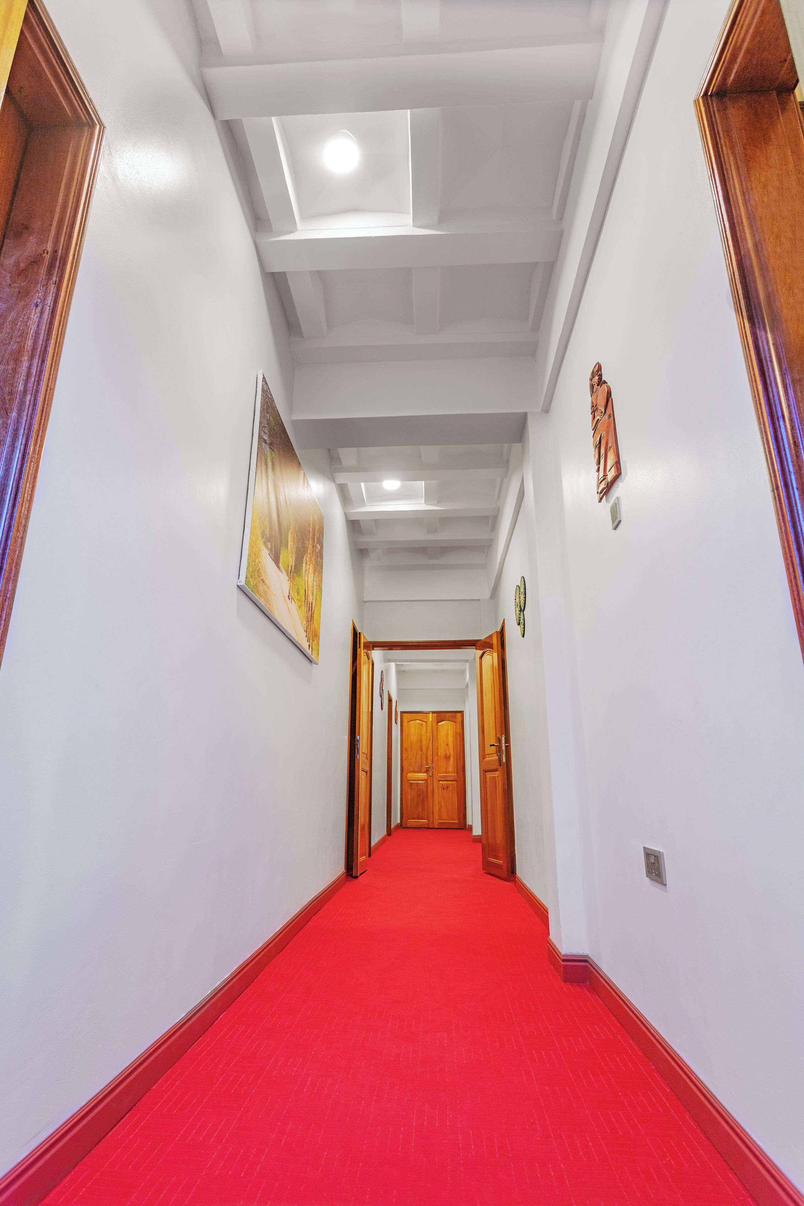 Un pasillo con alfombra roja, paredes blancas y puertas de madera.