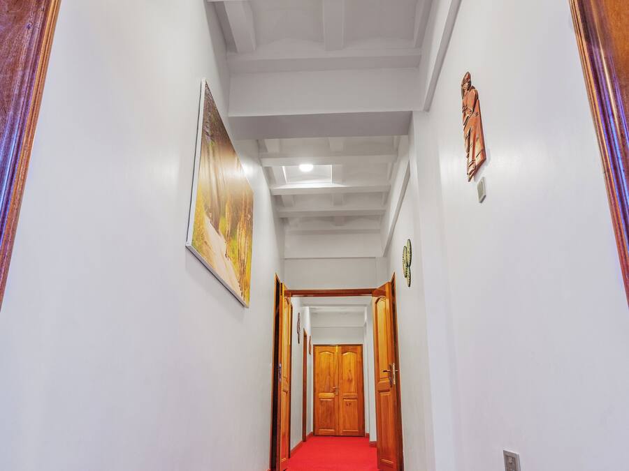 Un pasillo con alfombra roja, paredes blancas y puertas de madera.