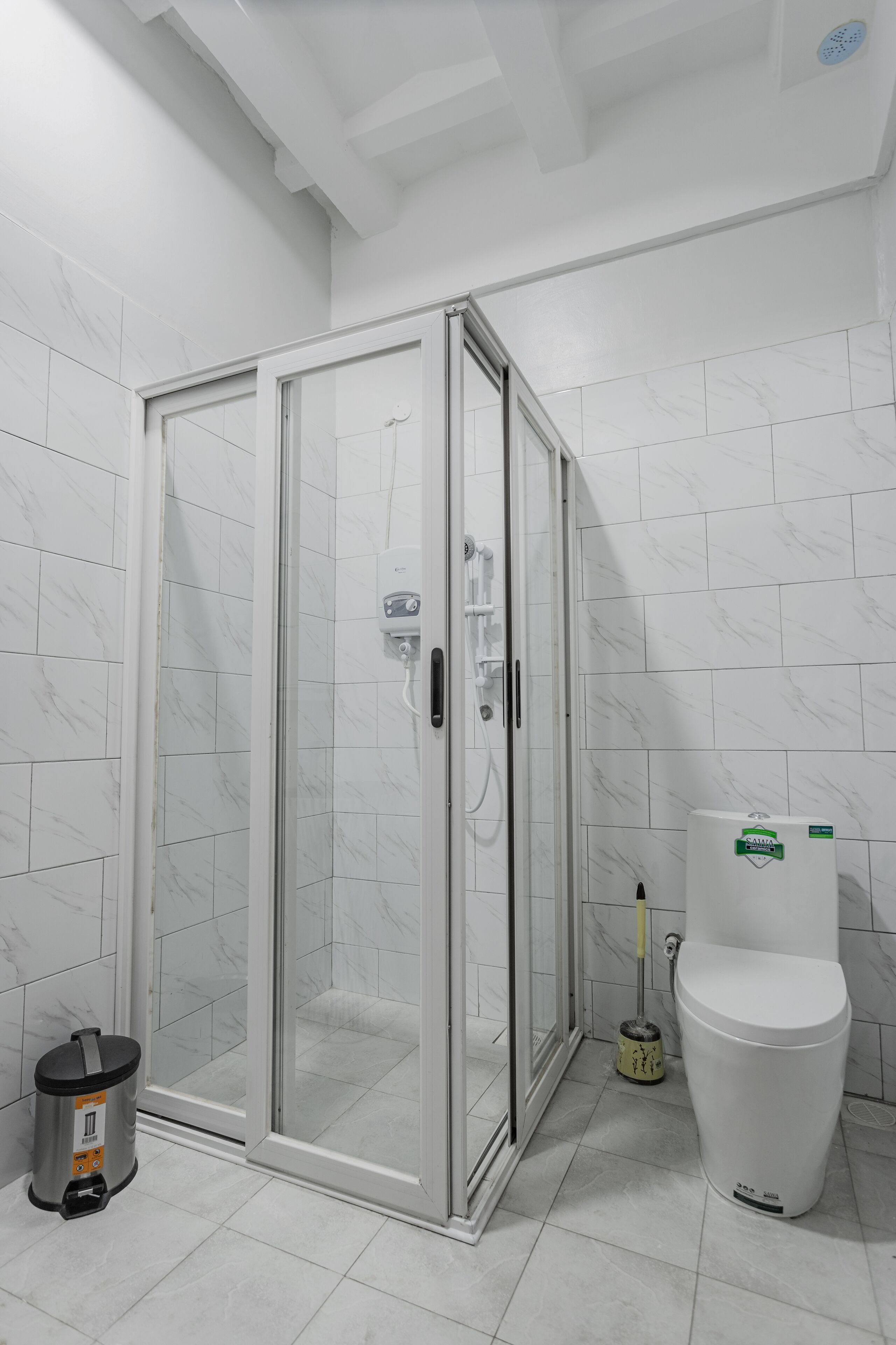 A bathroom with a glass-enclosed shower, a toilet, and a trash bin.