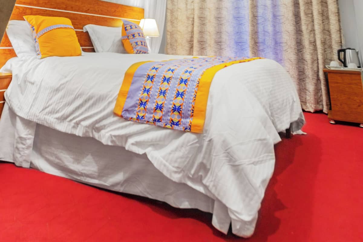 Quarto de hotel com cama, mesa de cabeceira, luminária e cortinas.