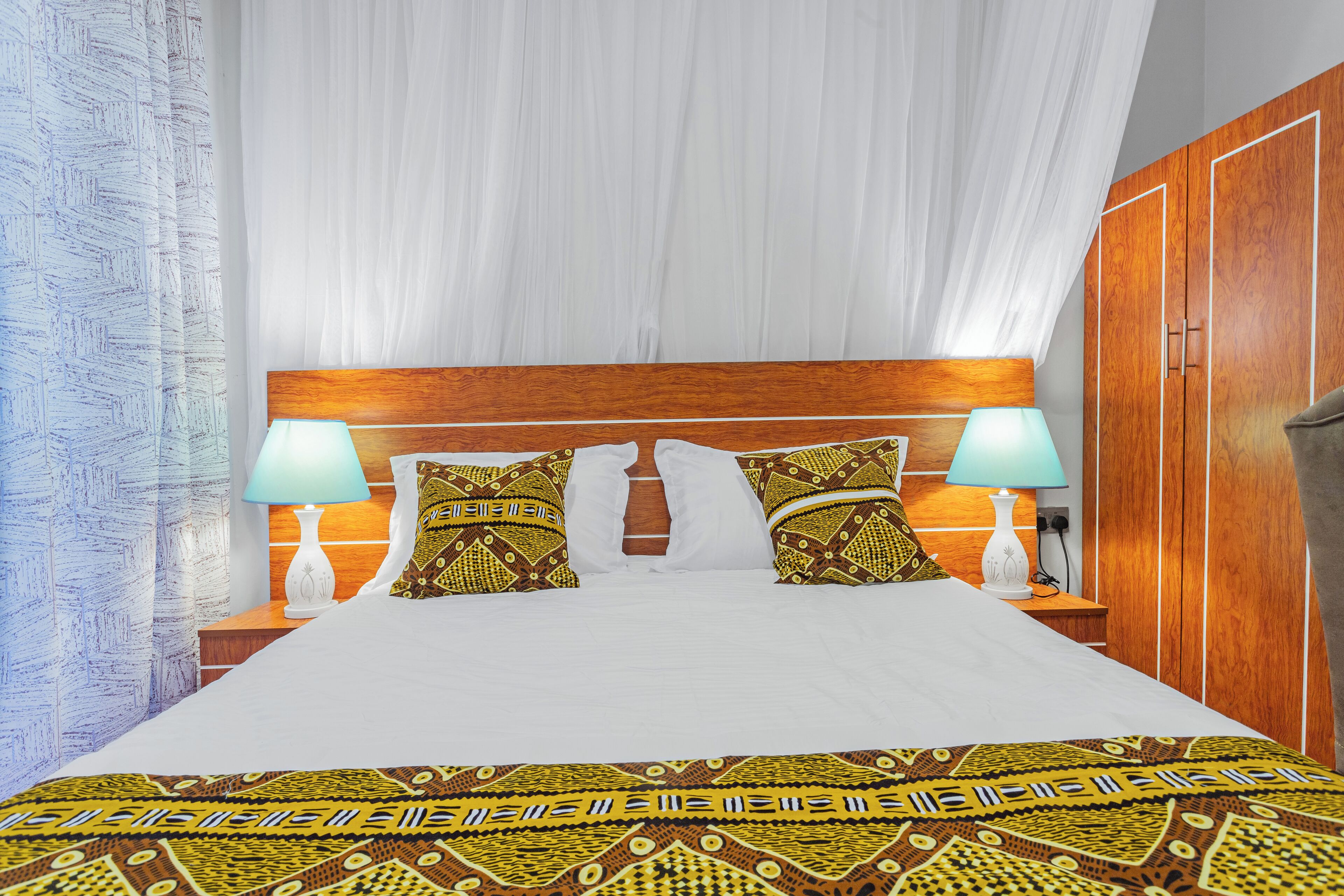 A bed with a wooden headboard, two bedside lamps, and patterned pillows.
