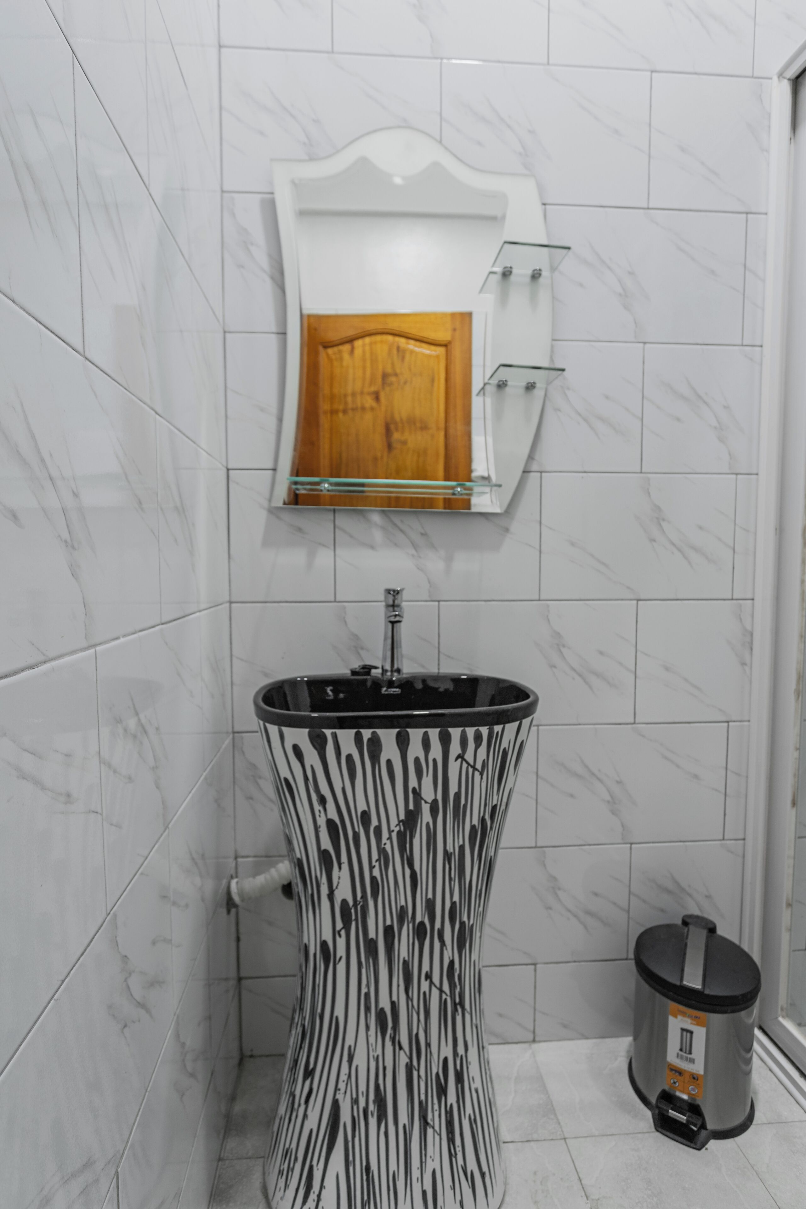 A bathroom with a marble-tiled wall, a wooden cabinet with a mirror, a black and white patterned sink, and a trash bin.