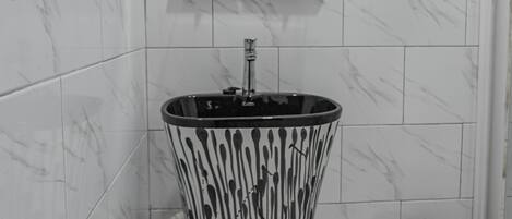 A bathroom with a marble-tiled wall, a wooden cabinet with a mirror, a black and white patterned sink, and a trash bin.