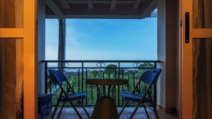 Ein Balkon mit zwei blauen Stühlen und einem gewebten Tisch, mit Blick auf eine üppige grüne Landschaft.