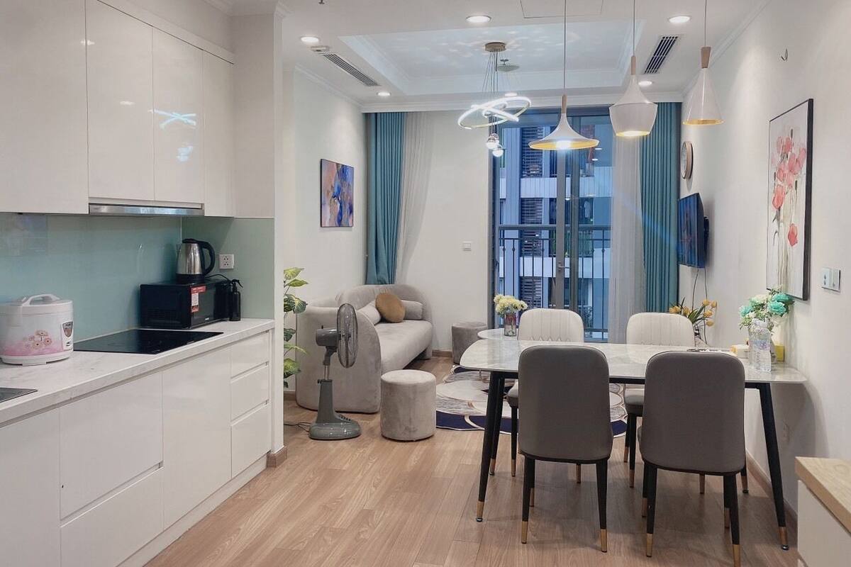 Eine moderne Küche mit weißen Schränken, ein Essbereich mit rundem Tisch und Stühlen sowie ein großes Fenster mit blauen Vorhängen.
