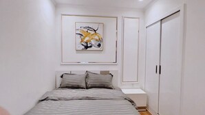 Une chambre à coucher comprenant un lit, une table de chevet, une armoire et un tableau abstrait encadré accroché au mur.