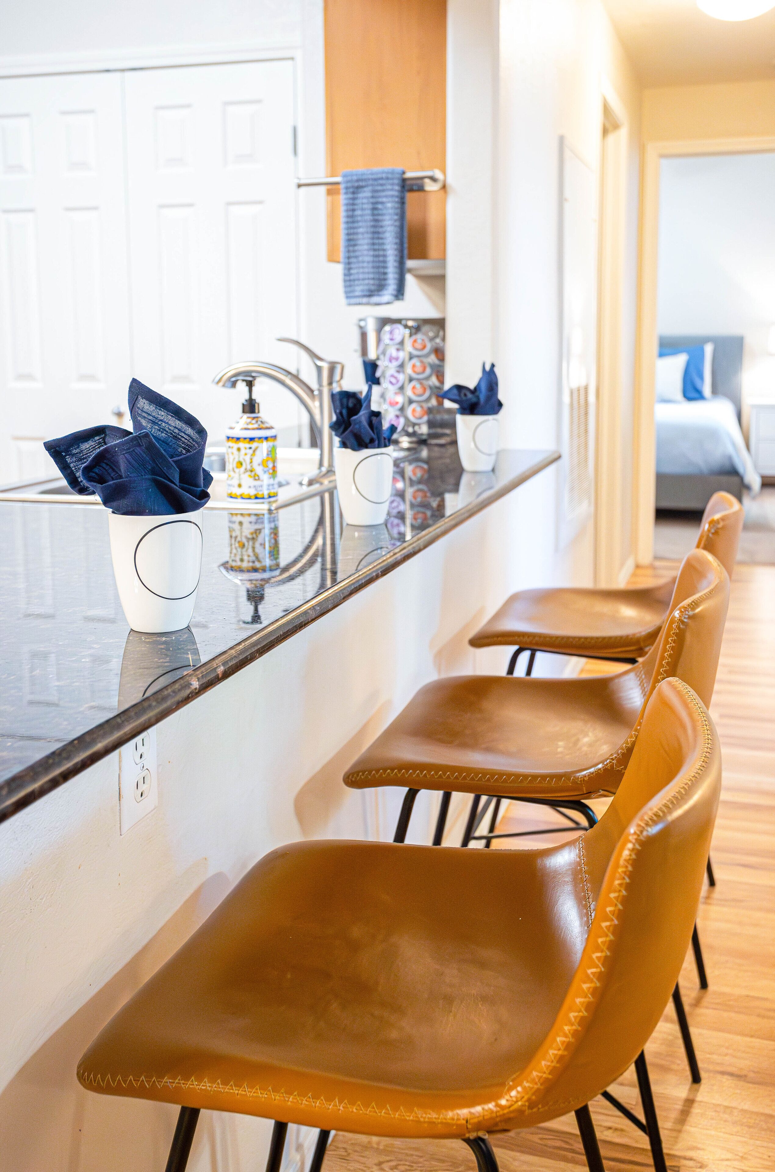 A kitchen with a long counter, four brown chairs, and a sink.