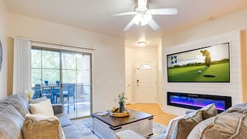 A living room with a large flat-screen TV, a ceiling fan, and a fireplace.