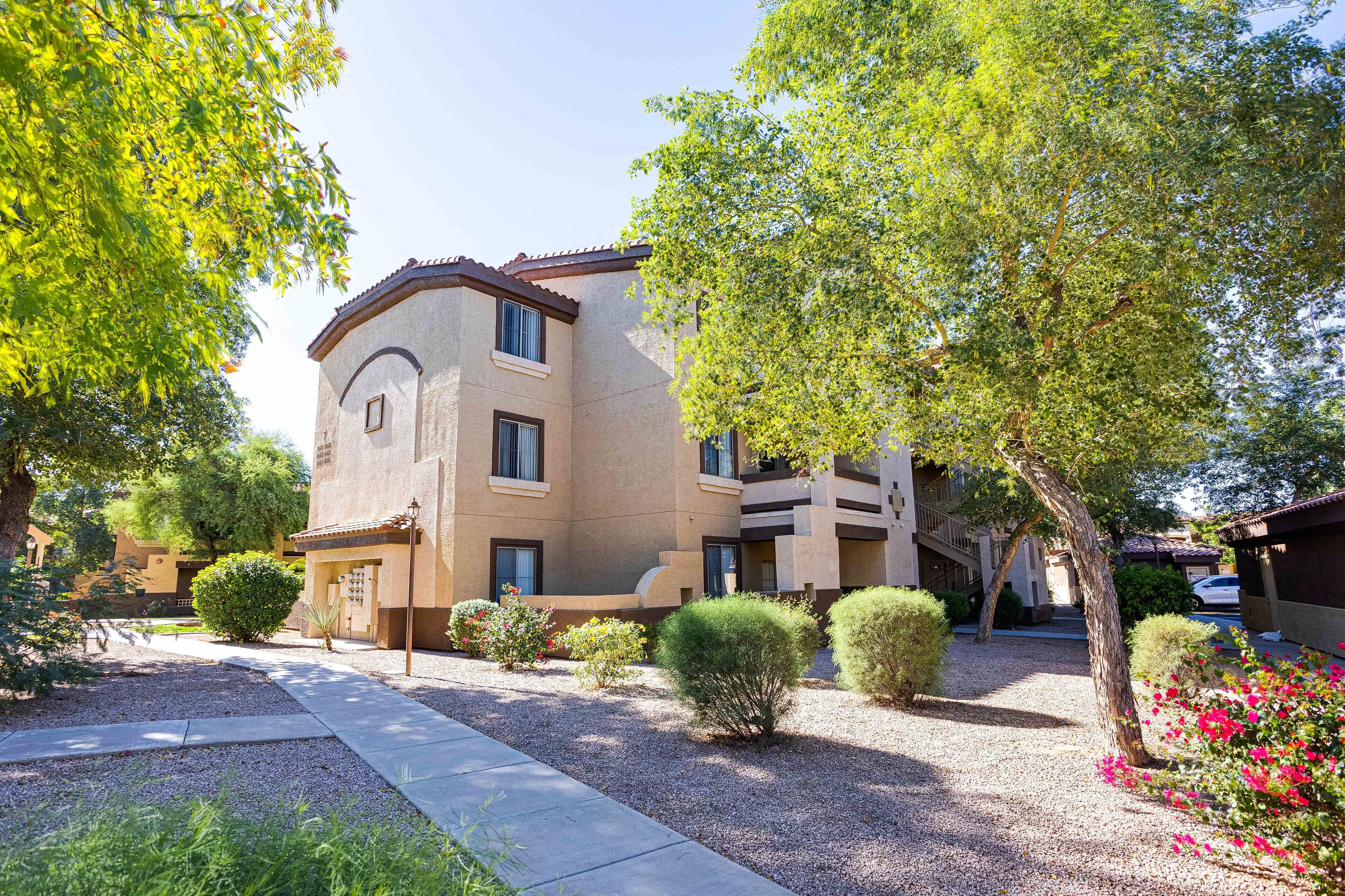 A multi-story building with a beige facade, surrounded by well-maintained landscaping and trees.