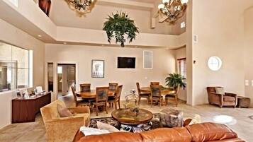 A spacious living room with a large brown leather sofa, a dining area with wooden chairs, and a chandelier.