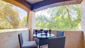 Une terrasse couverte, aménagée avec des meubles en osier et une table en verre, donnant sur un jardin.