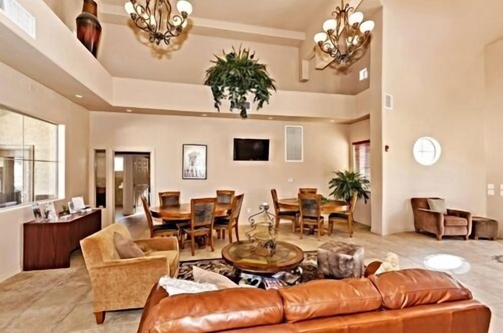 A spacious living room with a large brown leather sofa, a dining area with wooden chairs, and a chandelier.