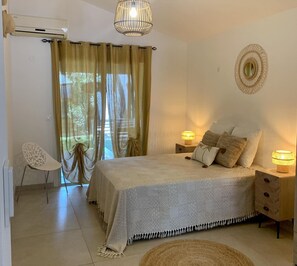 A bedroom with a bed, bedside lamps, a chair, and a window with curtains. - Villa "rosa Palma" Piscine Chauffée à St Gilles les Bains (Saint Paul)