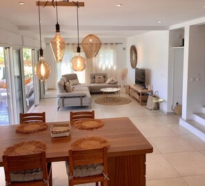 A modern living room with a sofa, TV, and dining area with a wooden table and chairs. - Villa "rosa Palma" Piscine Chauffée à St Gilles les Bains (Saint Paul)