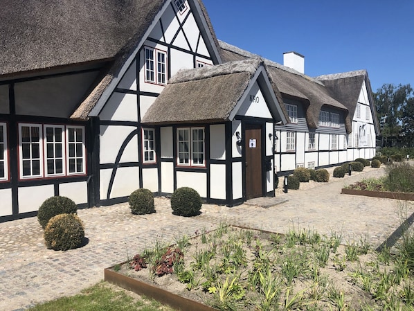 A traditional half-timbered building with a thatched roof, a cobblestone pathway, and a garden with various plants. - Hotel Nørrevang (Vaeggerlose)