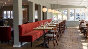 A restaurant with a long red bench, wooden tables, and hanging pendant lights. - Hotel Nørrevang (Vaeggerlose)