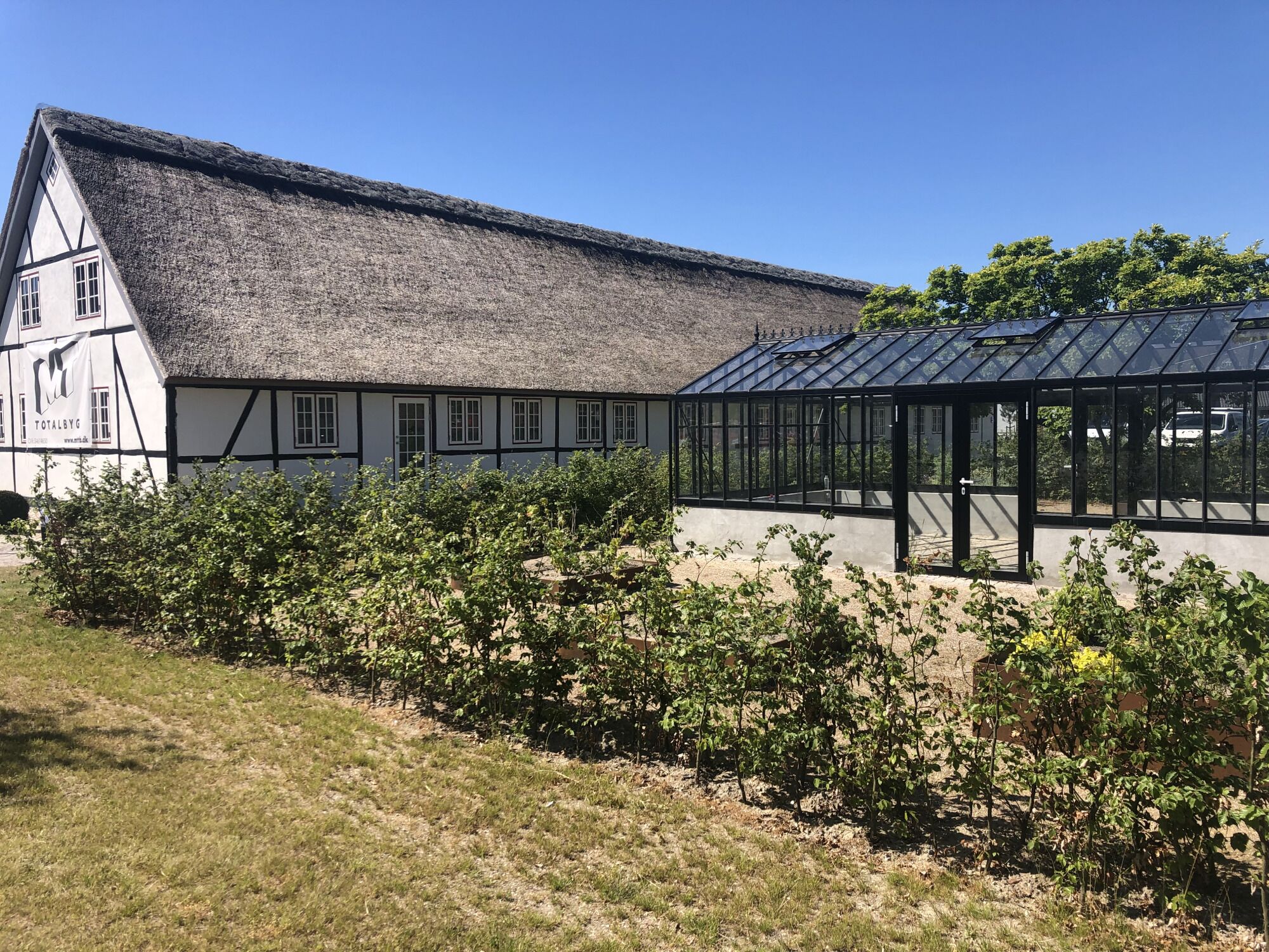 A traditional building with a thatched roof and a modern glass greenhouse structure.