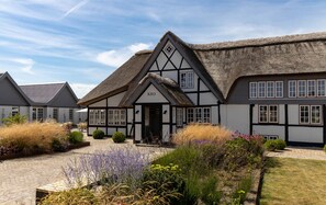 A traditional half-timbered house with a thatched roof, a sign reading "KRO", and a paved courtyard with various plants and shrubs. - Hotel Nørrevang (Vaeggerlose)