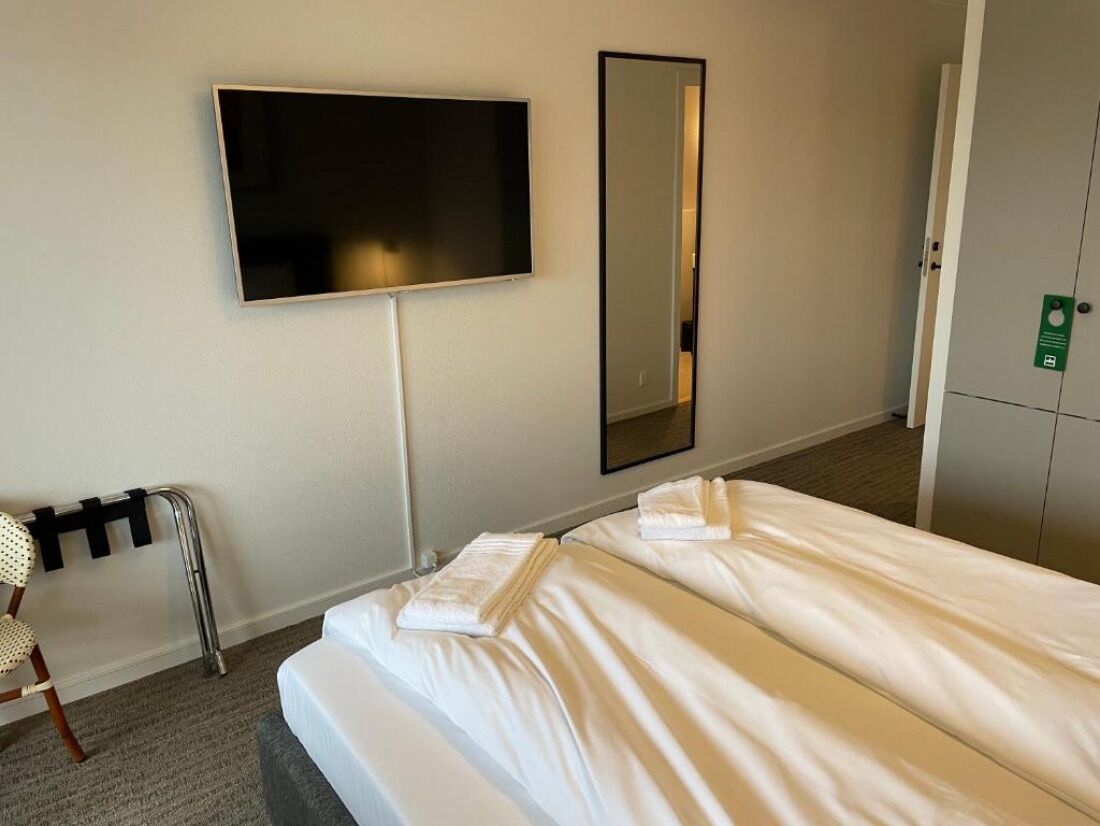 Quarto de hotel com cama, uma cadeira, televisão e espelho.