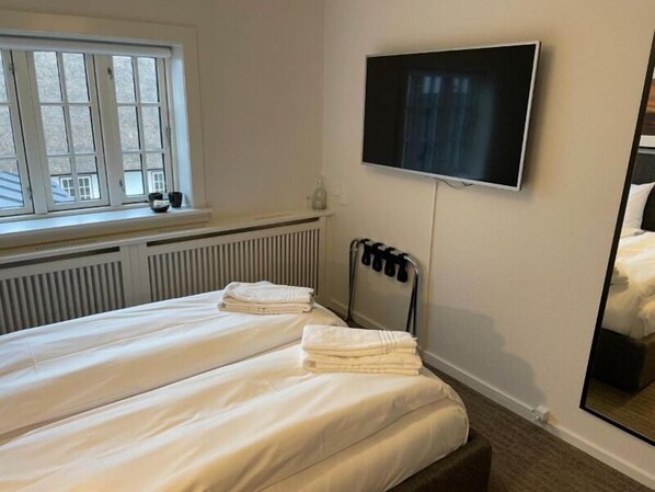 A hotel room with two beds, a TV mounted on the wall, a window with blinds, and a radiator. - Hotel Nørrevang (Vaeggerlose)