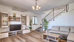 Un soggiorno moderno con televisione a schermo piatto, parquet, un divano, un tavolino da caffè e una scala.