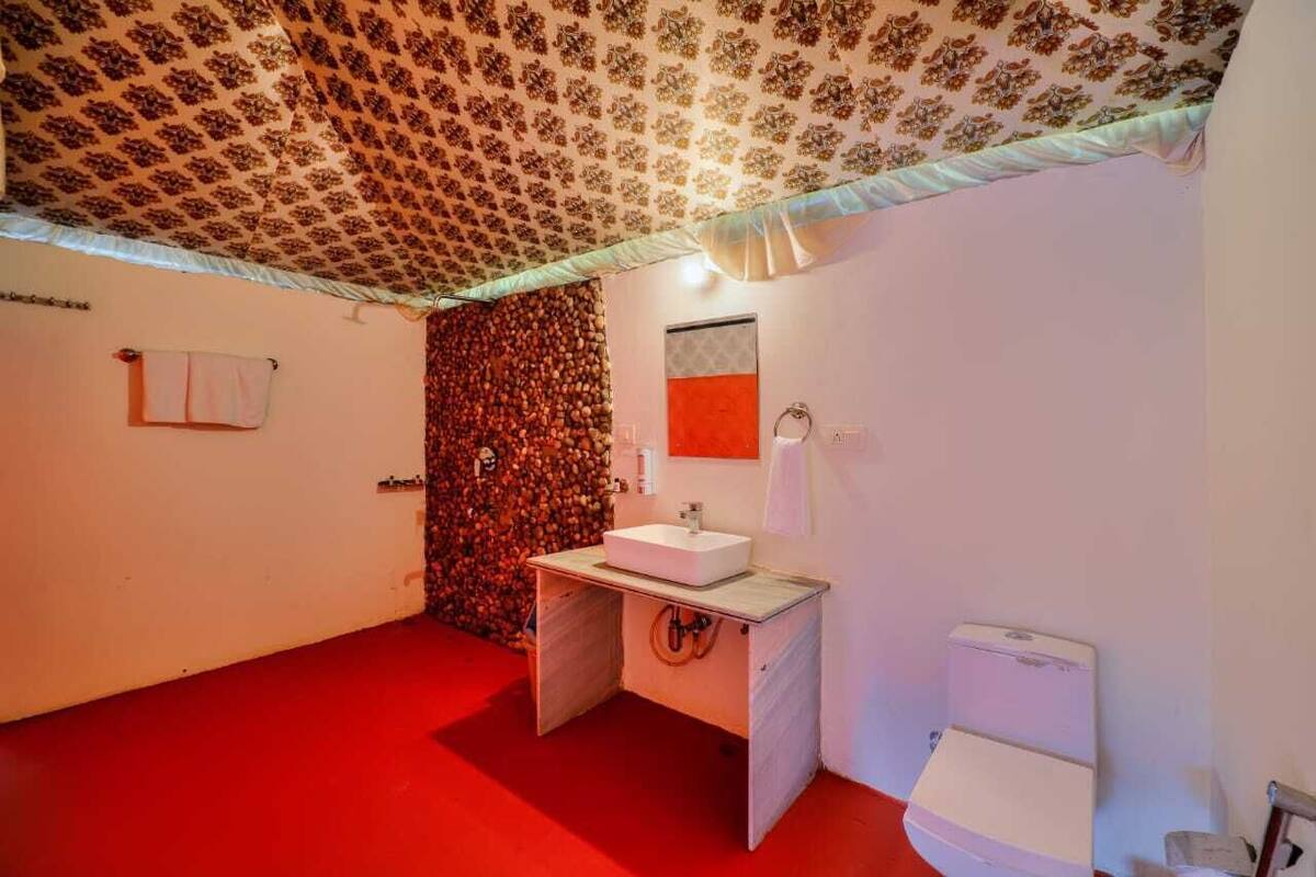 A bathroom with a red floor, a white sink, a toilet, and a patterned ceiling.