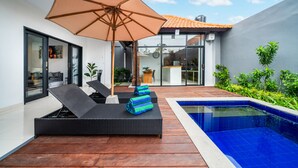 Un espace piscine extérieur moderne, doté de chaises longues, d’un grand parasol et d’une terrasse en bois.