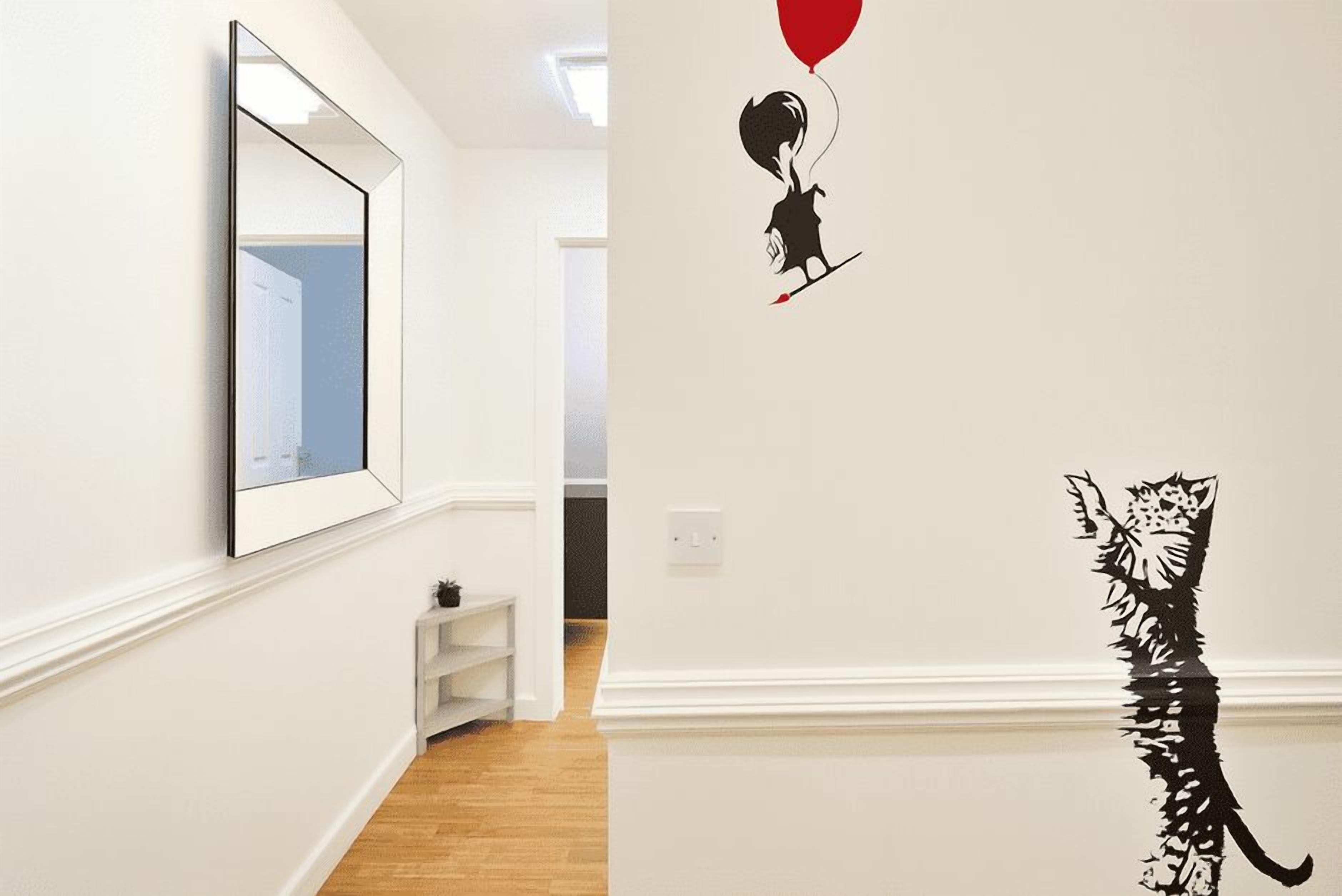 Un couloir avec un miroir sur le côté gauche, un autocollant représentant un chat sur le mur, et une porte blanche au fond.