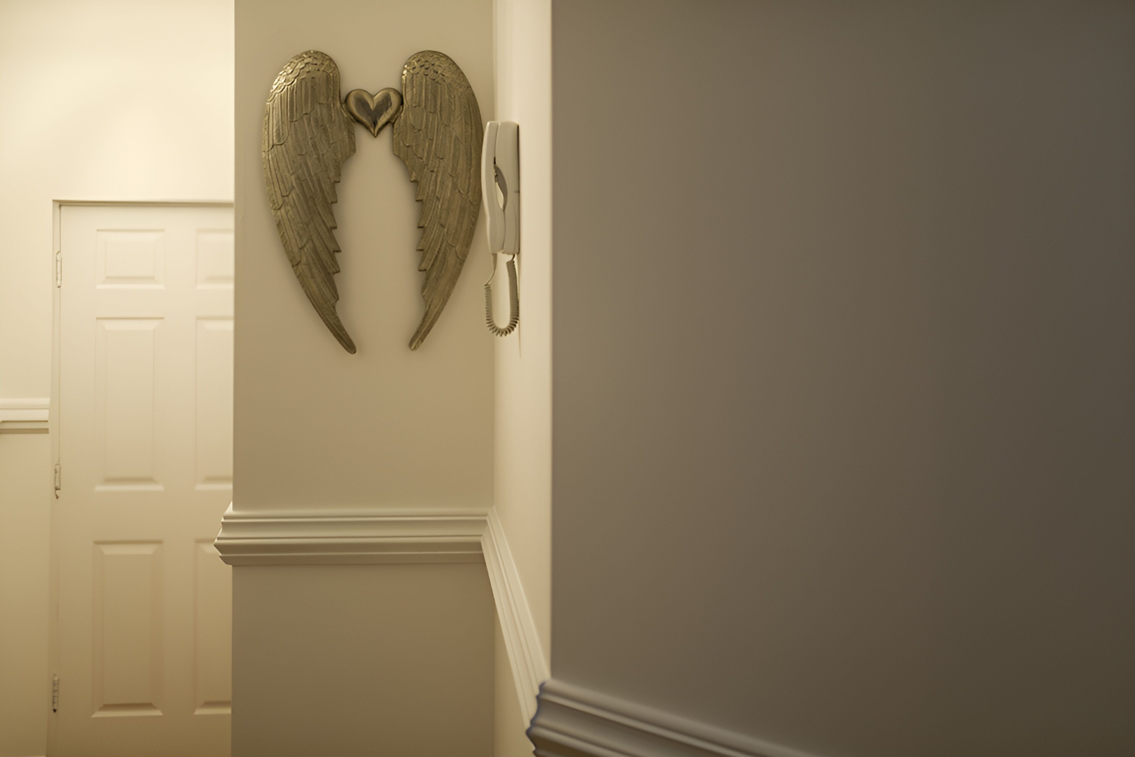 A hallway with a white door, a wall-mounted telephone, and a decorative angel wing.
