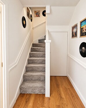 A staircase with carpeted steps leading to a white door, surrounded by walls with vinyl records and framed artwork.