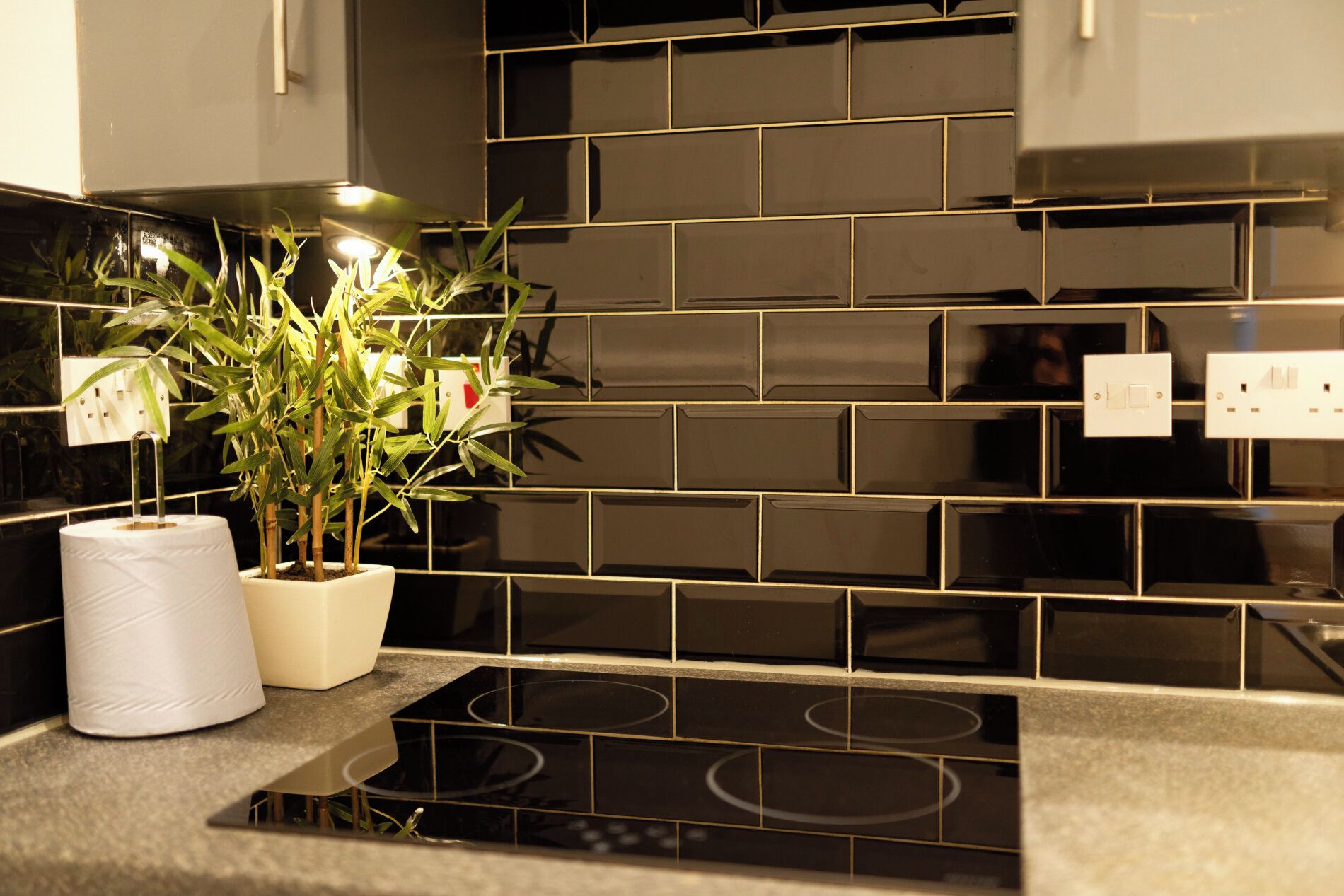 A kitchen with black tiled backsplash, a stove, and a potted plant on the counter.