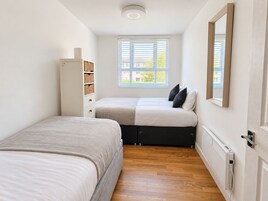 A compact bedroom with two beds, a wardrobe, a window with blinds, and a radiator.