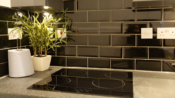 A modern kitchen with black tiled backsplash, a built-in stove, and a potted plant. - White Tulip Central 3bedroom Duplex Loft (Liverpool)