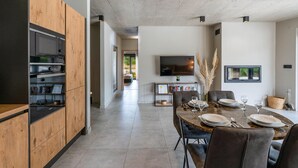 A modern kitchen with wooden cabinets and built-in appliances, a dining area with a marble table, and a living space with a flat-screen TV and bookshelves. - Stunning home in Pula (Pula)