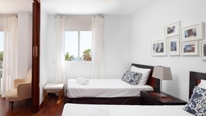 Habitación de hotel con dos camas, una silla, una mesita y una ventana con cortinas.