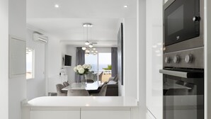 A modern kitchen with a built-in oven, a dining area with a table and chairs, and a view of the sea through large windows. - Chaparral Seafront by Alfresco Stays (Mijas Costa)