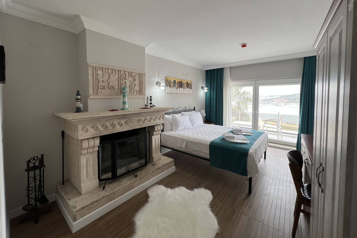 A bedroom with a fireplace, a bed, a balcony with a view, and a dining area.