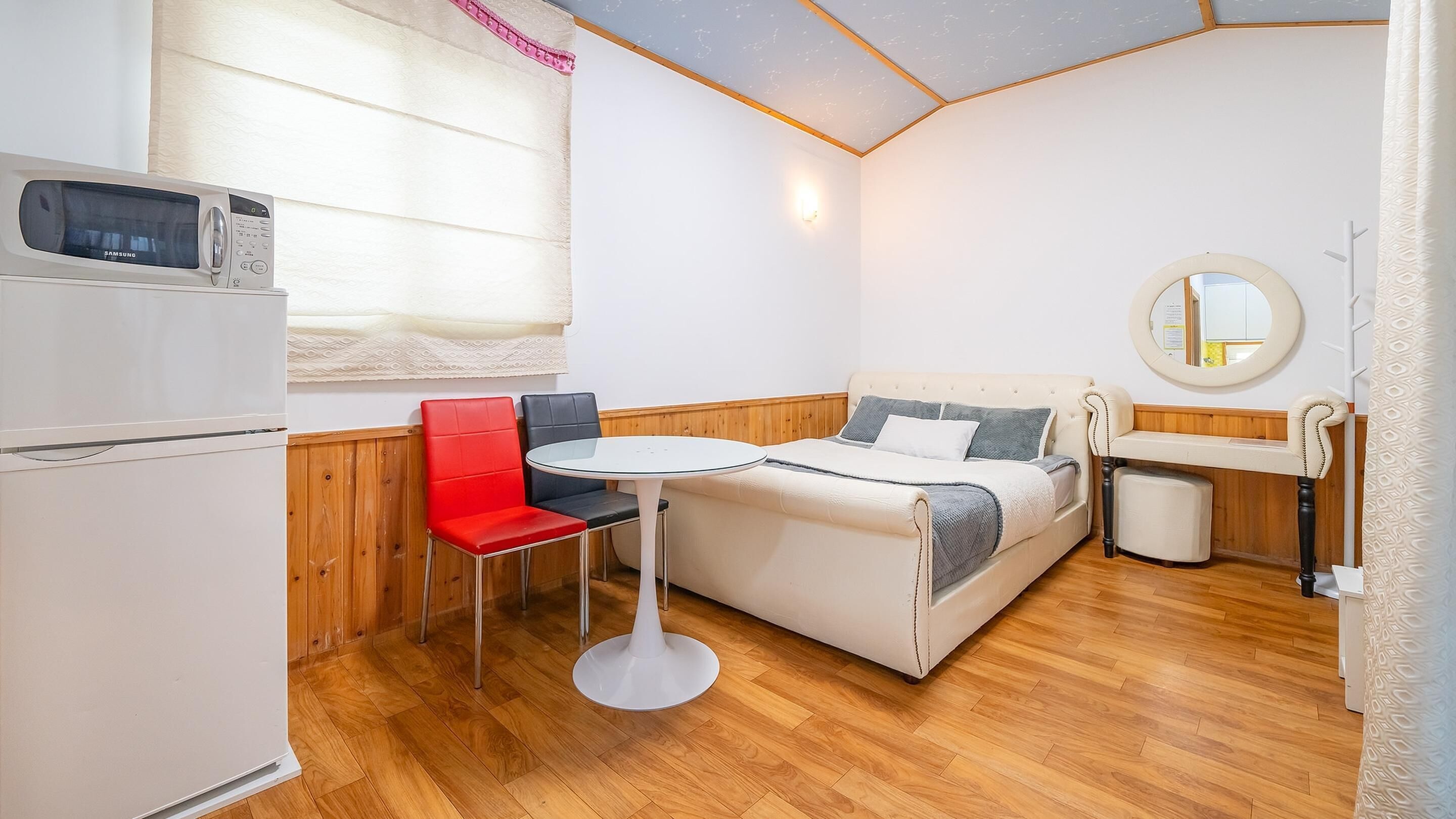 A compact room with a kitchenette, a bed, a round dining table, and a red chair.