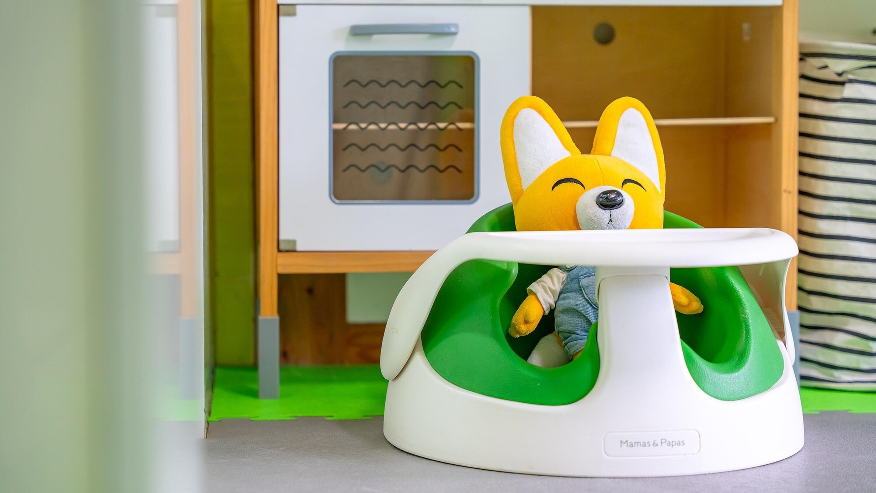 A baby rocker with a plush toy rabbit, a storage cabinet, and a striped pillow.