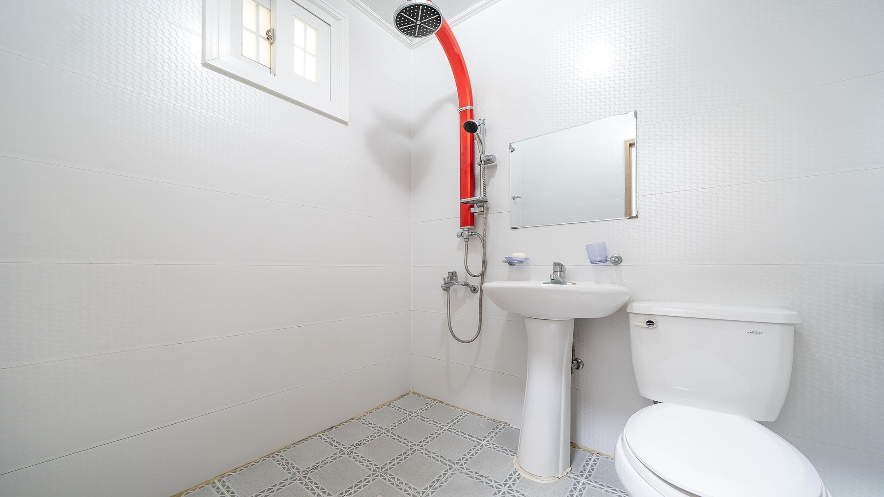 Un baño con lavamanos, inodoro y ducha con manguera roja.