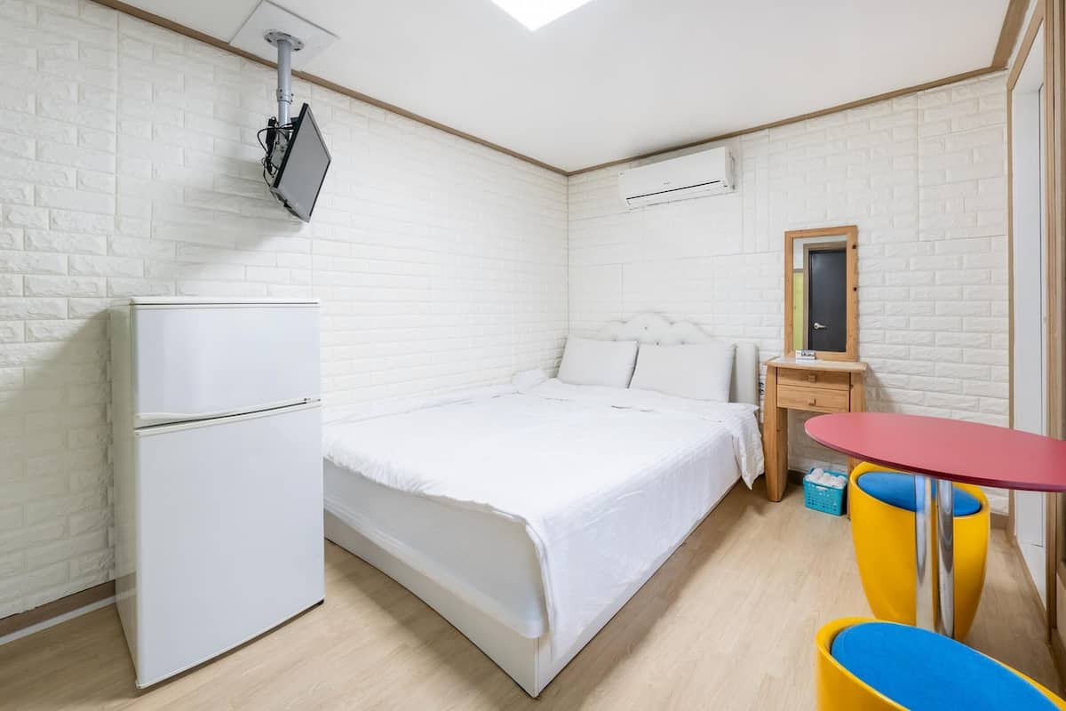 A compact room with a bed, a small desk, a refrigerator, and a window with a view.